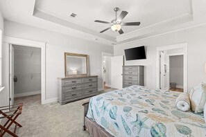 A bedroom with a bed, dresser, mirror, ceiling fan, and TV.
