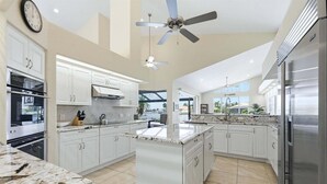 A modern kitchen with white cabinetry, a central island, a ceiling fan, and a view of the outdoors. - Punta Gorda Isles Vacation Home with Private Pool on Canal with a Boat Dock (Punta Gorda)
