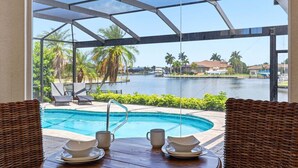 A pool area with a view of a body of water, lounge chairs, and a dining table with plates and cups. - Punta Gorda Isles Vacation Home with Private Pool on Canal with a Boat Dock (Punta Gorda)
