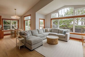 Ein modernes Wohnzimmer mit Ecksofa, Esstisch und großen Fenstern.