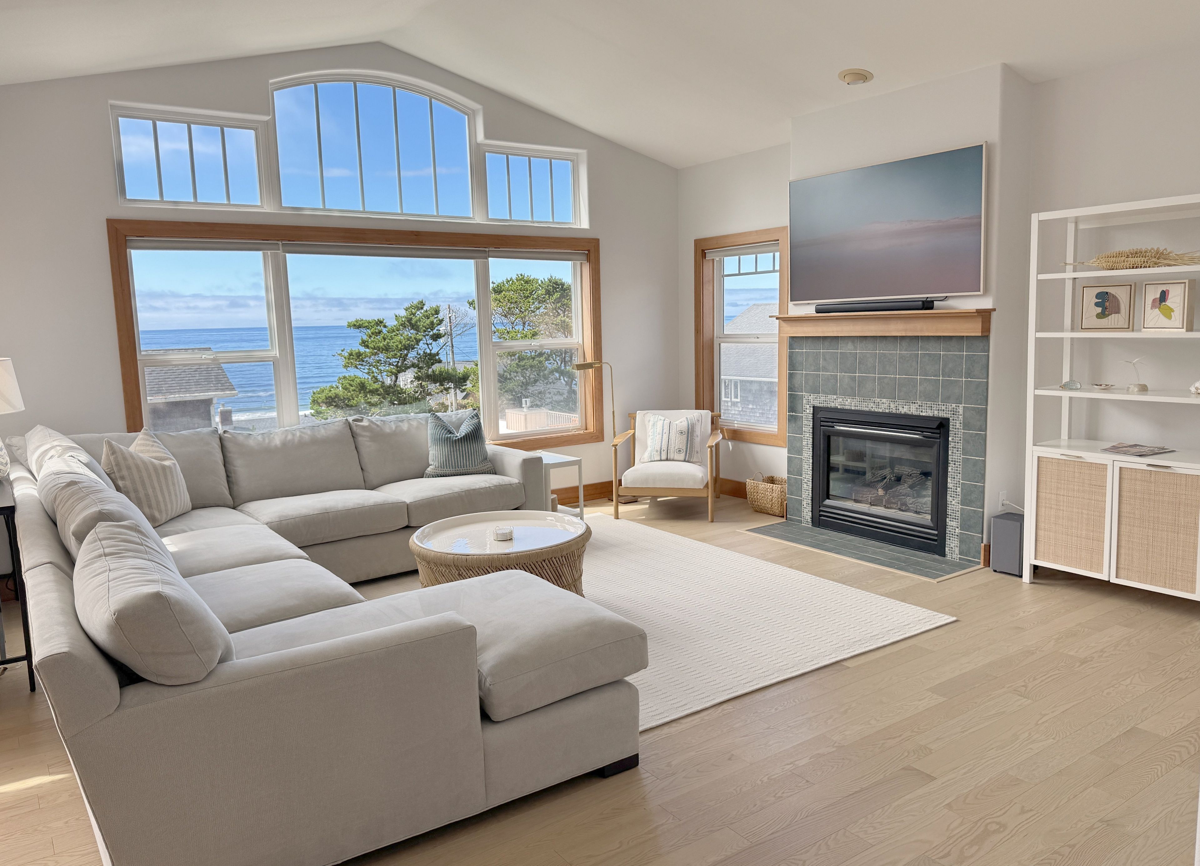 Ein modernes Wohnzimmer mit einer großen Couch, einem Kamin, einem Fernseher und Meerblick.