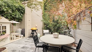 Un patio con una mesa redonda y sillas, una parrilla y una zona de estar cubierta.