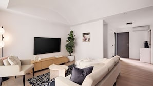 Una sala de estar moderna con una televisión de pantalla plana, un sofá, una mesa de centro, una planta en maceta y un diseño minimalista.