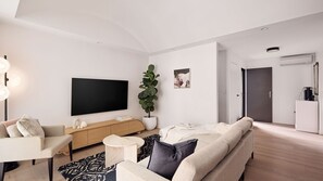 A modern living room with a flat-screen TV, a sofa, a coffee table, a potted plant, and a minimalist design. - Ivy Terrace, Annandale IH (Annandale)