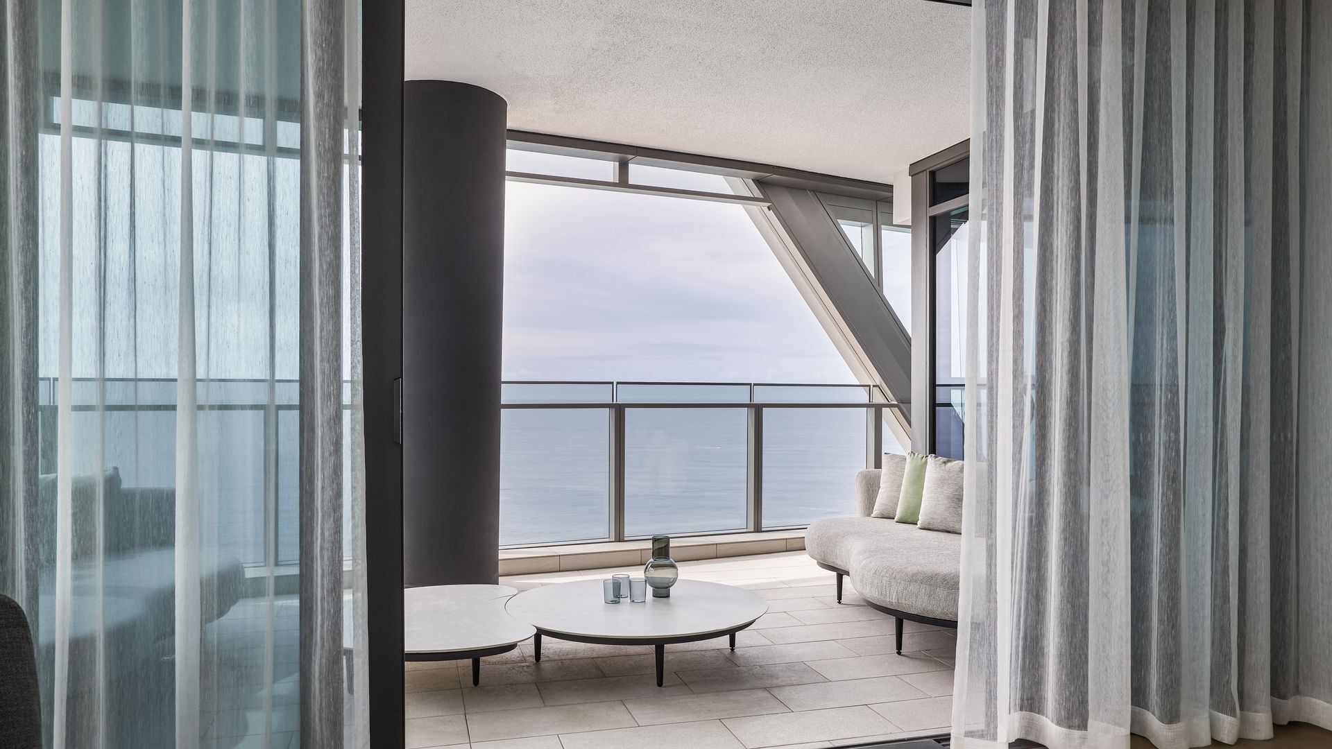 Ein moderner Balkon mit Meerblick, ein runder Tisch mit einer Vase und eine Couch mit Kissen.