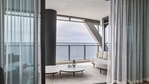 En moderne balkon med havudsigt, et rundt bord med en vase, og en sofa med puder.