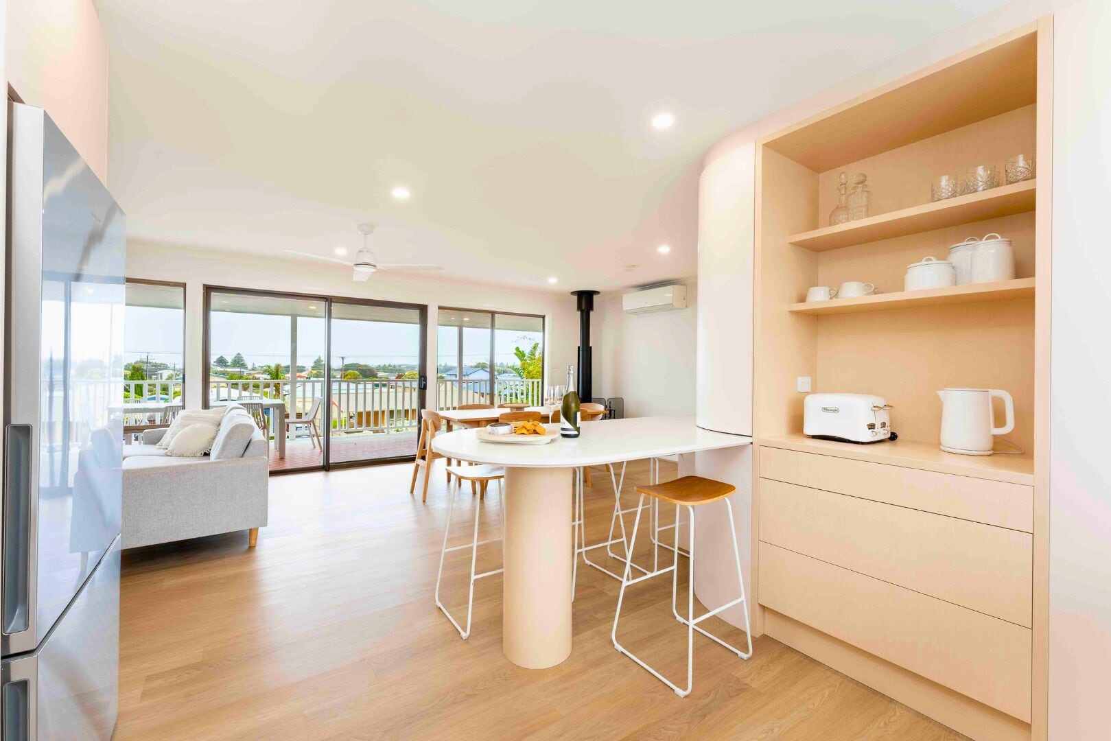A modern kitchen with a dining area, a large window with a view, and a built-in shelf with kitchenware.