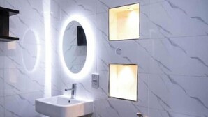 A bathroom with a white sink, a large mirror with a circular light, and two square wall lights. - The Luxe Stay, 2 Bed Room Apartment (Lagos)