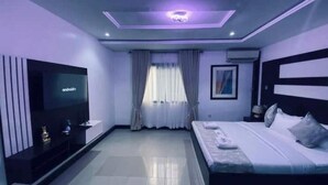 A modern bedroom with a bed, a TV, a ceiling light, and a window with curtains. - The Luxe Stay, 2 Bed Room Apartment (Lagos)