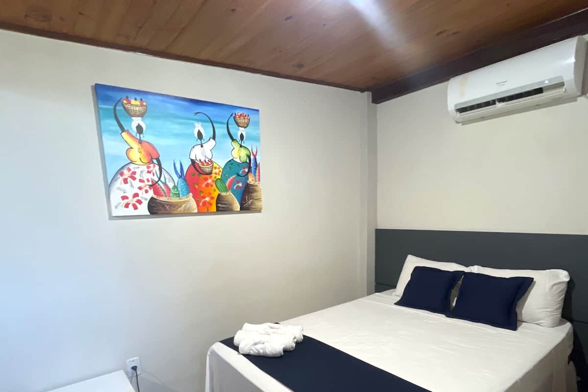 Un dormitorio con cama, un cuadro, un calentador blanco y un aire acondicionado de pared.