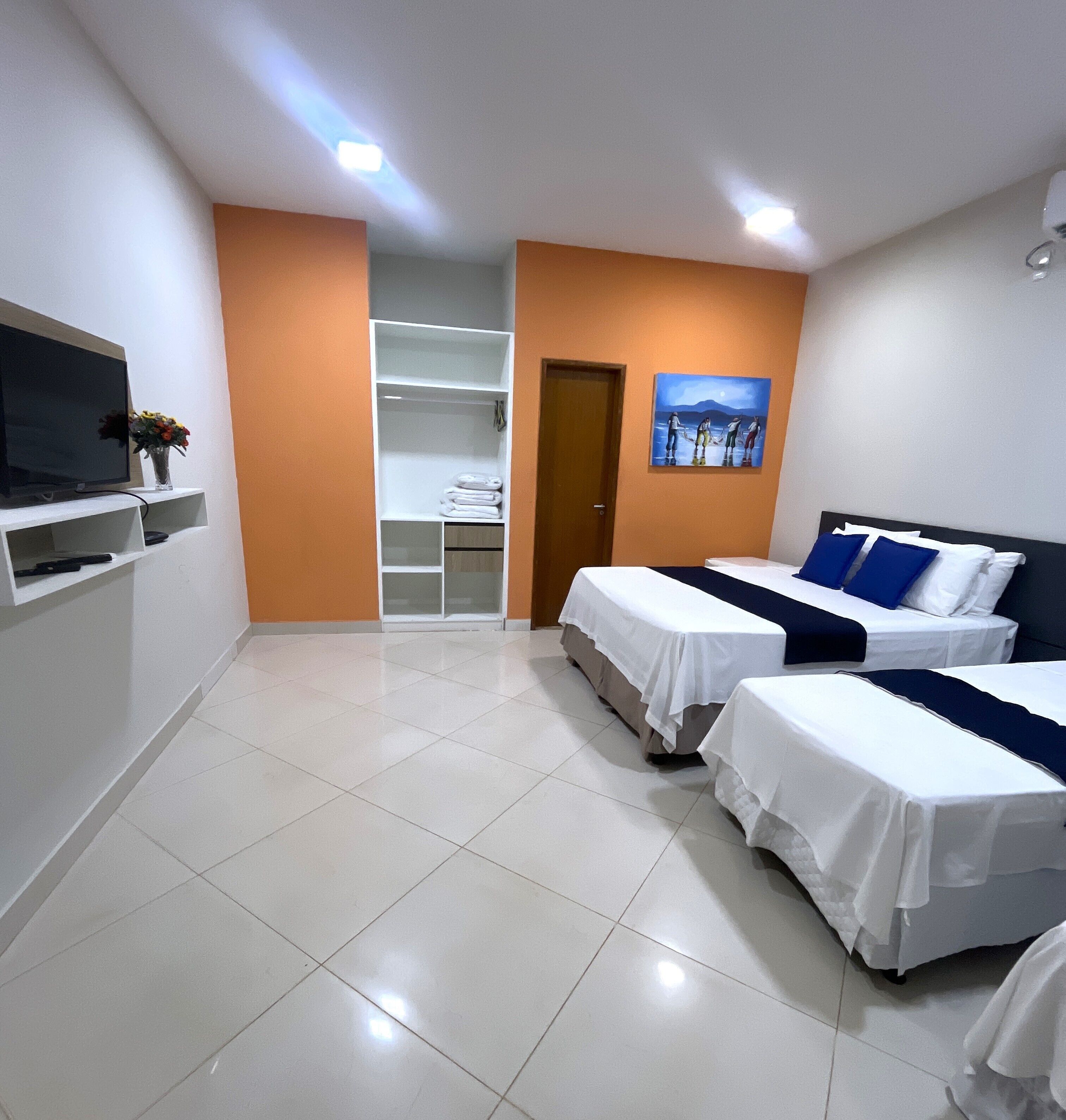 A hotel room with two beds, a TV, a wardrobe, and a painting on the wall.