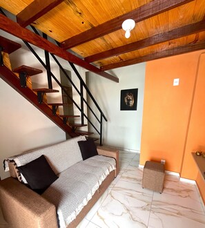 A room with a wooden staircase, a sofa with patterned cushions, a framed picture on the wall, and a tiled floor. - Pousada Bugaendrus Paradise (Touros)