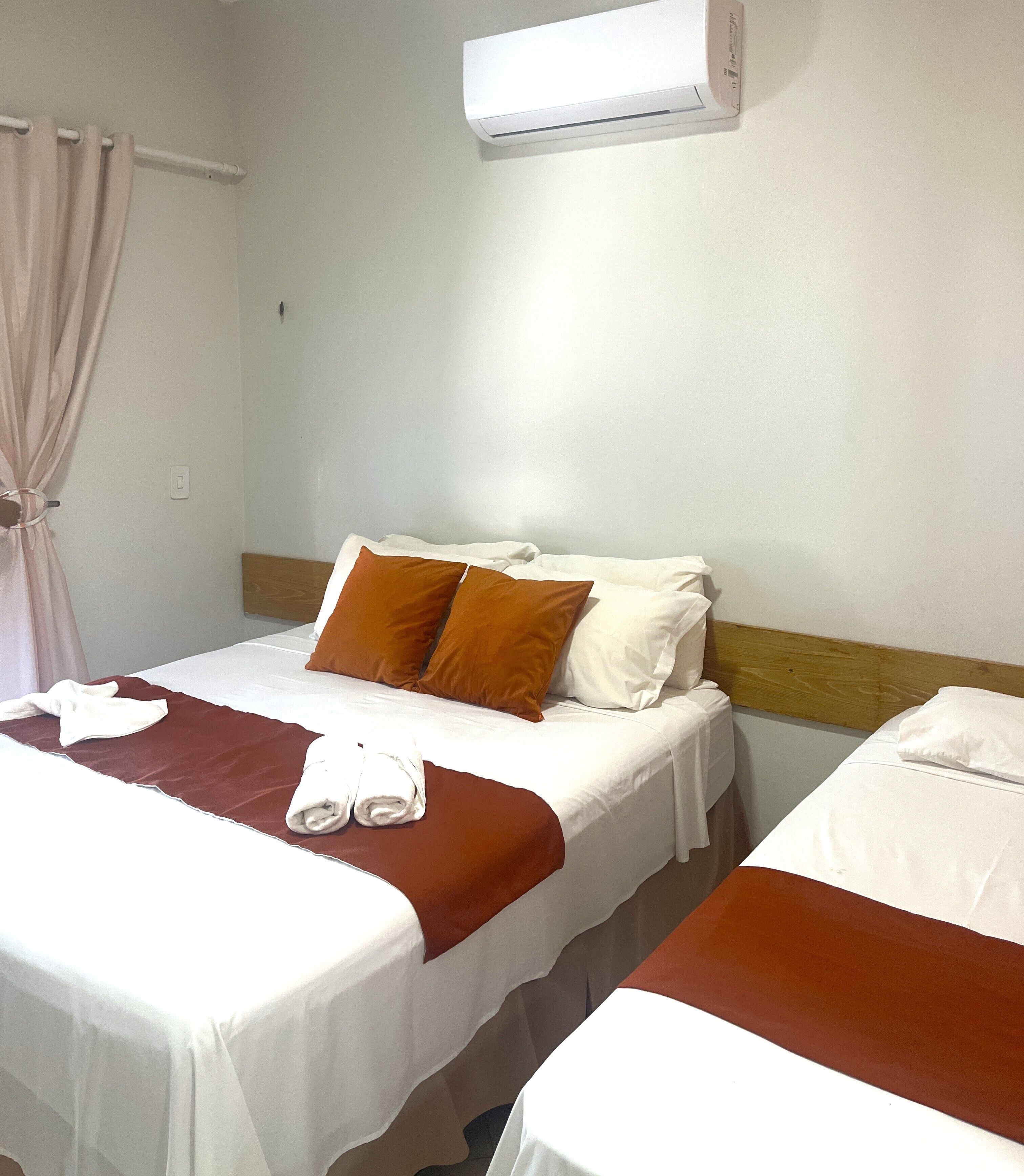 A hotel room with two beds, a wooden headboard, a white air conditioning unit, and a curtain.