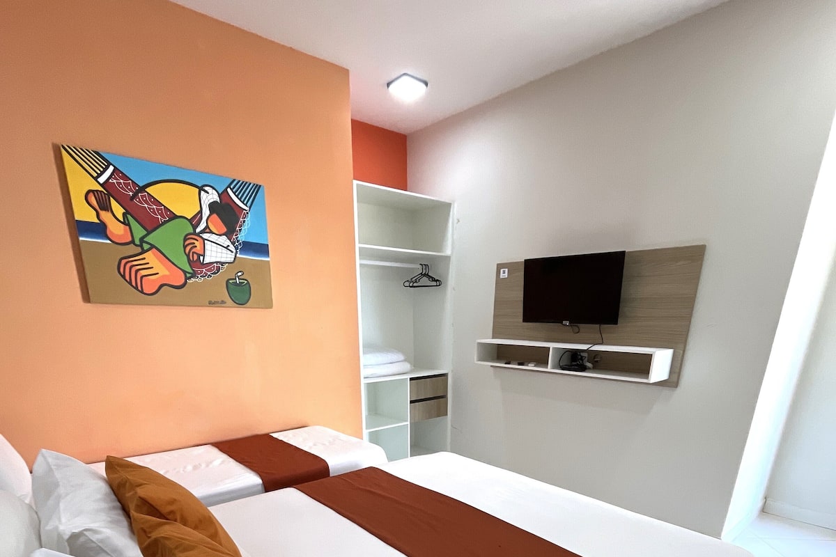 Habitación de hotel con dos camas, un televisor montado en la pared y un cuadro.