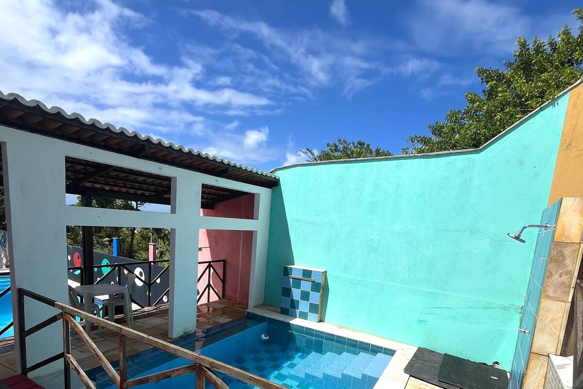 Una piscina con solárium de baldosas, un área techada con sillas y vista al cielo.