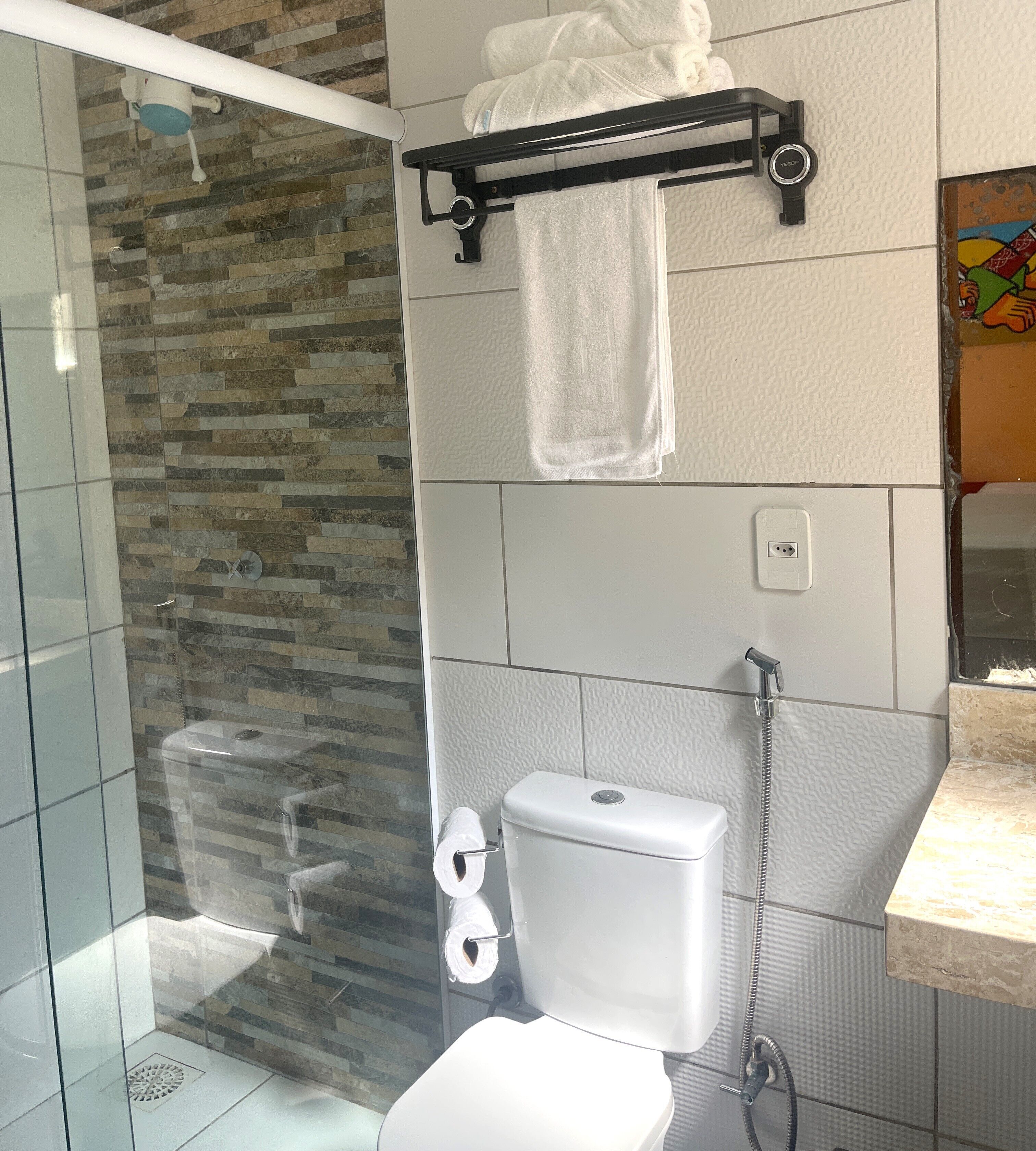 Un baño con cabina de ducha de vidrio, inodoro con dispensador de toallas de papel y barra para toallas con toallas.
