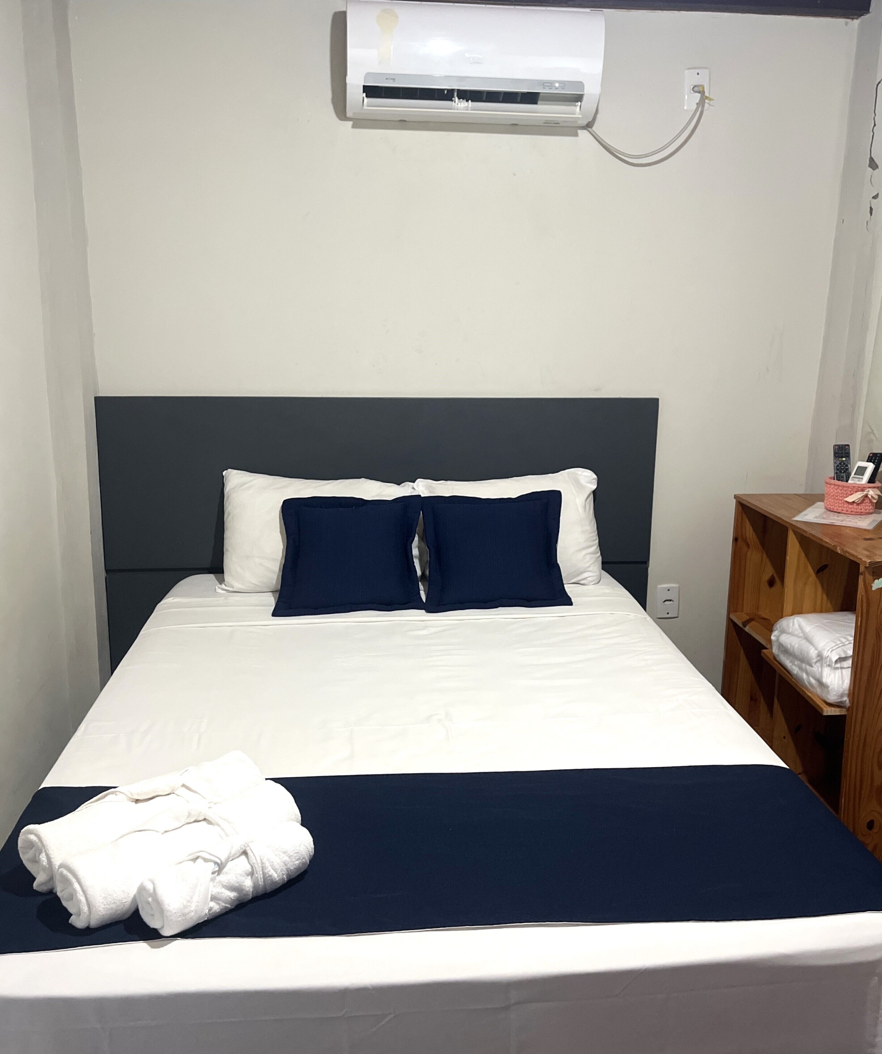 Una cama individual con cabecera oscura, ropa de cama blanca y almohada azul decorativa.