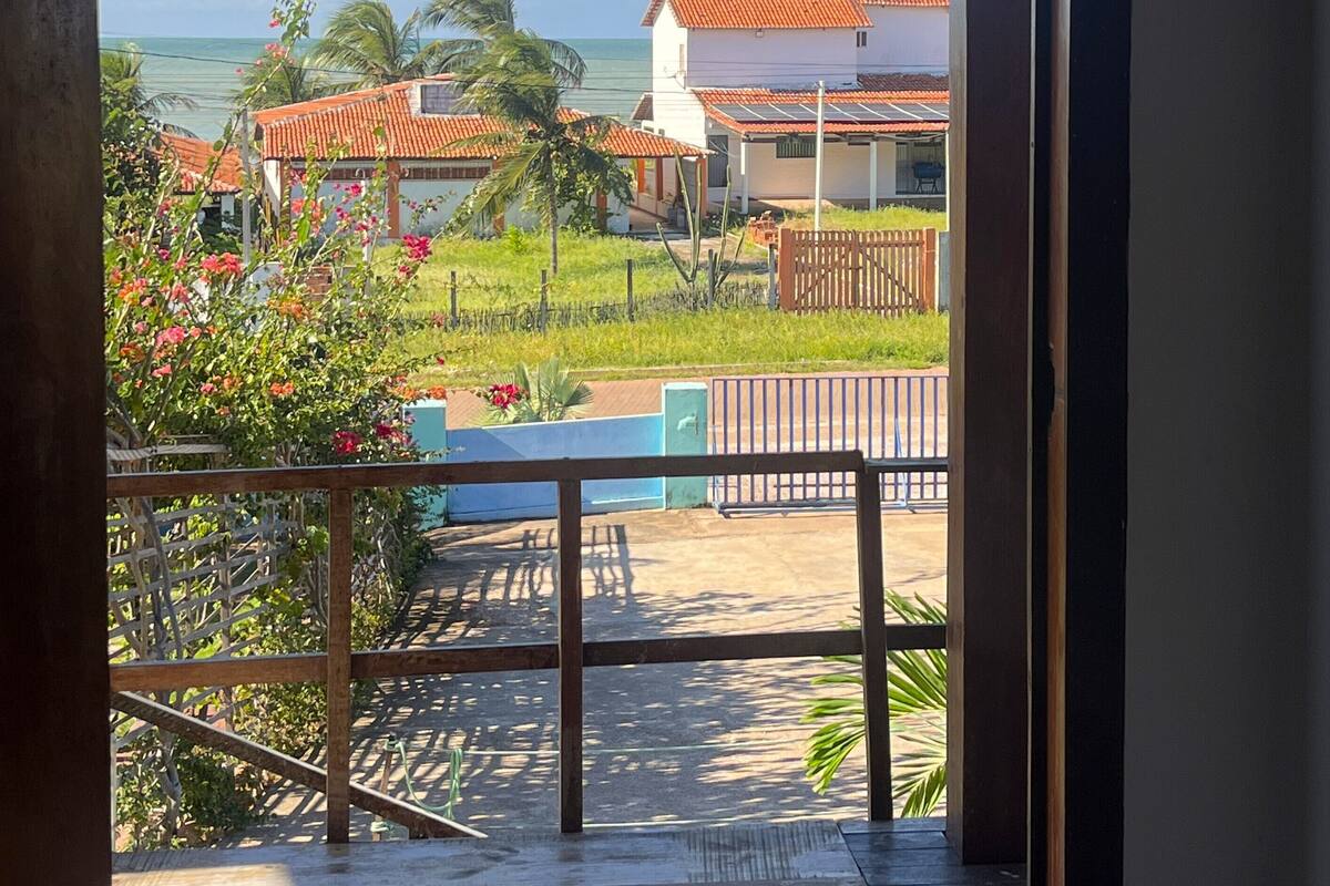 Vista a través de una ventana que muestra un edificio con tejado de baldosas, un espacio exterior cercado y un cielo despejado.