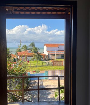 A view through a window of a building with a tiled roof, a fenced outdoor area, and a clear sky. - Pousada Bugaendrus Paradise (Touros)