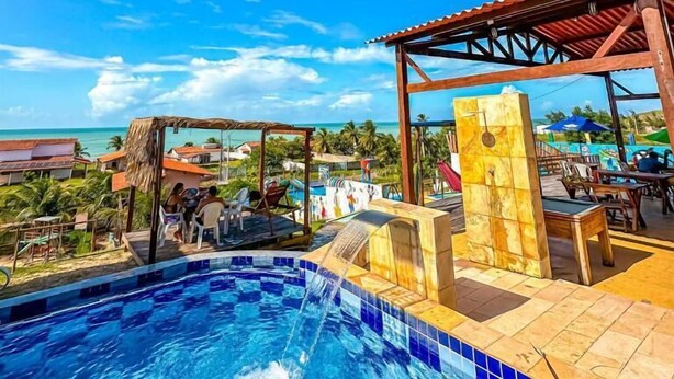 A pool area with a view of the ocean, a covered seating area, and a building with a tiled facade.