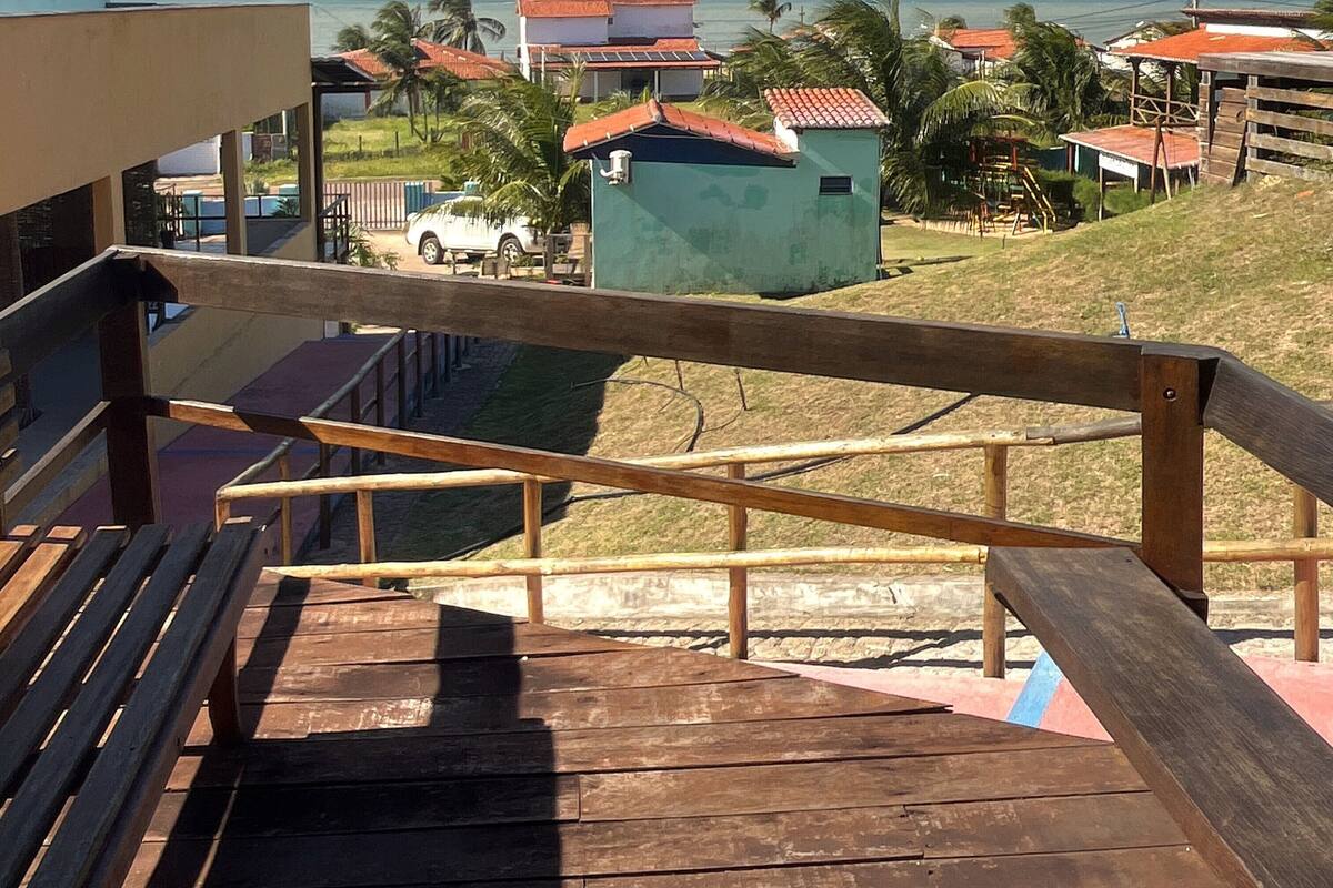Una escalera de madera conduce a un balcón con vistas a la costa, casas y palmeras.
