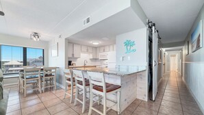 A modern kitchen with a large island, bar stools, and a view of the outside. - Island Winds East 311 | Walk to the Hang Out | Beachview | My Beach Getaways (Gulf Shores)