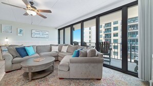 A modern living room with a sectional sofa, a coffee table, and a ceiling fan. - Island Winds East 311 | Walk to the Hang Out | Beachview | My Beach Getaways (Gulf Shores)