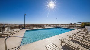 A clear blue sky with a bright sun, a swimming pool, and sun loungers. - Island Winds East 311 | Walk to the Hang Out | Beachview | My Beach Getaways (Gulf Shores)