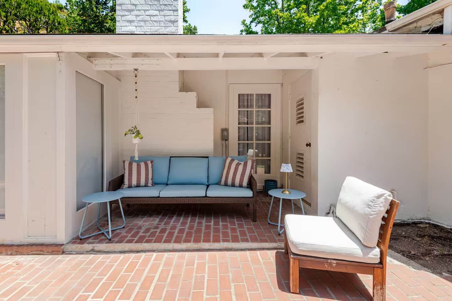 A covered patio with a blue sofa, a wooden chair, and a small table.