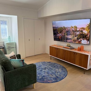 Ein Wohnzimmer mit einem Flachbildfernseher, einem grünen Sofa, einem gemusterten Teppich und einem Retro-Kühlschrank.