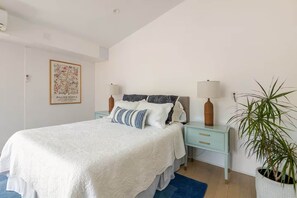 A bedroom with a bed, two bedside tables, a nightstand, a potted plant, and a framed picture on the wall. - 90210 NEST: Private Pool Retreat in Beverly Hills (Beverly Hills)