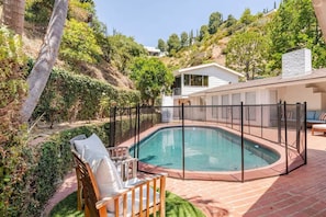 Ein Schwimmbecken mit Zaun, Stuhl und einem Haus im Hintergrund.
