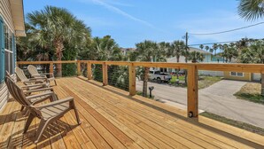 Un terrazza in legno con sedie, una ringhiera e vista su una strada con palme e case.