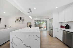 A modern kitchen with white cabinetry, a marble island, and a stainless steel refrigerator. - Spacious 4 Bedroom House W/ Amazing Backyard (Chula Vista)