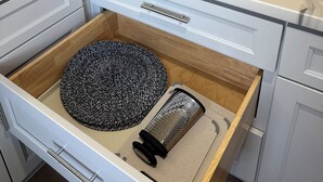 Een keuken met een marmeren aanrecht, een lade met een rasp en een rek voor koffiemokken.