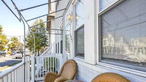 Eine Veranda mit Korbmöbeln, einem weißen Geländer und einem großen Fenster, das Gebäude widerspiegelt.
