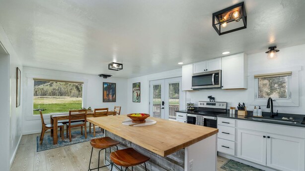 Una cocina moderna con una isla de madera, armarios blancos y un ventanal con vistas a un área verde.