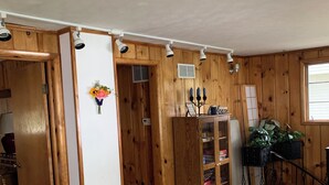 Una habitación con paredes de madera, una puerta blanca, un armario, una estantería, una planta y una ventana.