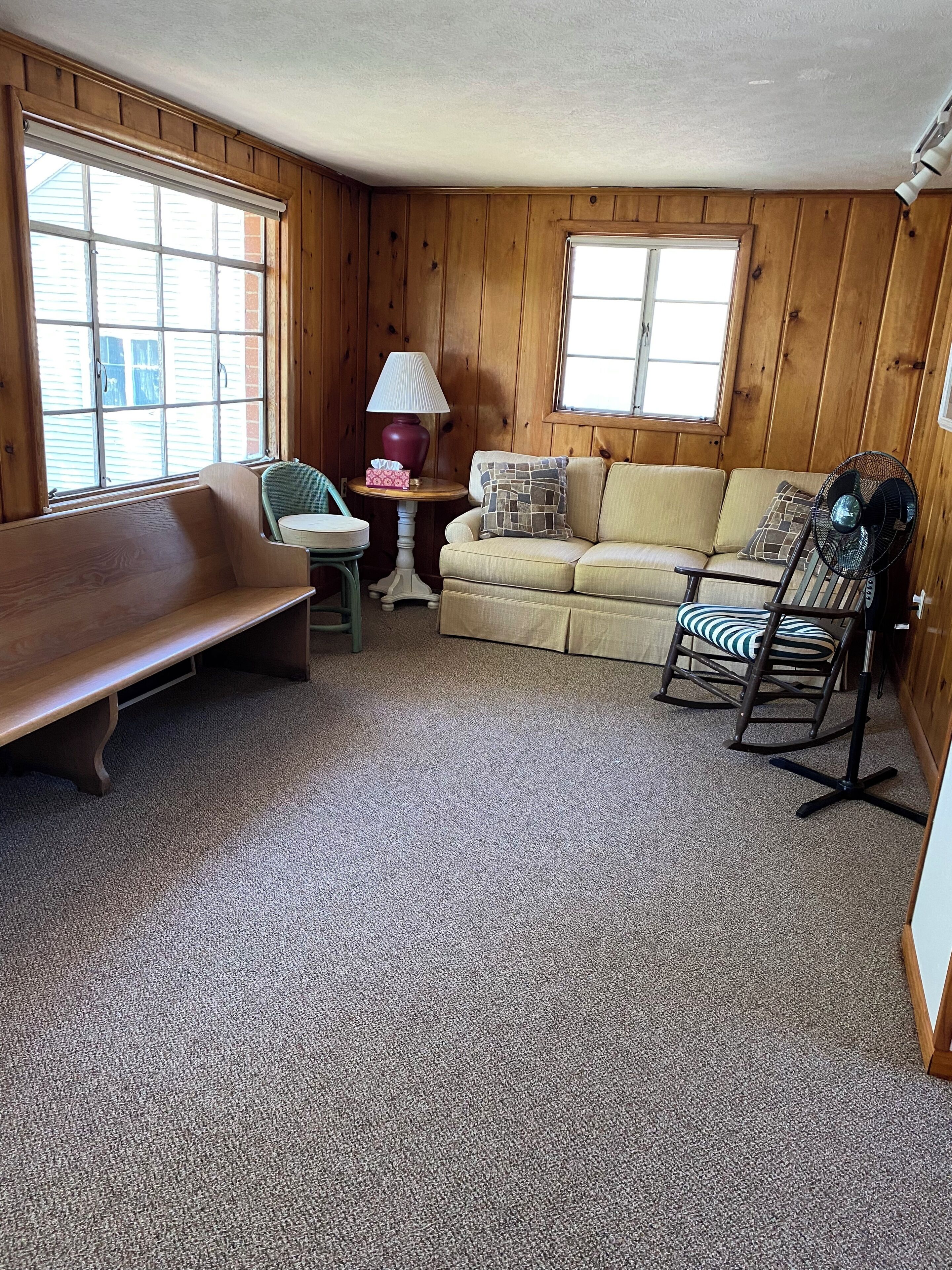 A cozy room with a wooden bench, a small table with a lamp, a sofa, and a rocking chair.