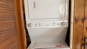 Una unidad compacta de lavadora y secadora con panel de control, ubicada en una habitación con piso de madera y una puerta.