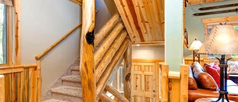 Un escalier en bois avec un palier recouvert de moquette, une porte en bois et une lampe posée sur une table.