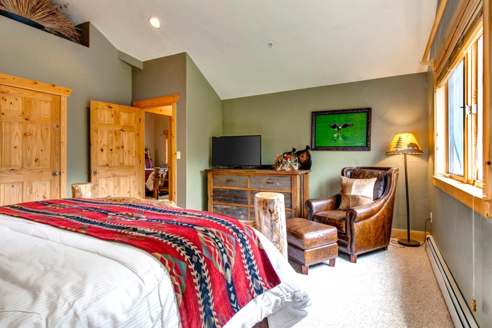 A bedroom with a bed, a desk, a chair, a television, and a window.