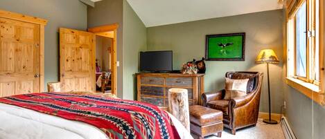 A bedroom with a bed, a desk, a chair, a television, and a window.