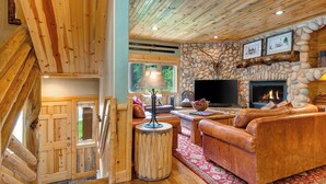 Ein rustikales Blockhaus-Interieur mit Kamin aus Stein, Ledersofa und Fernseher.