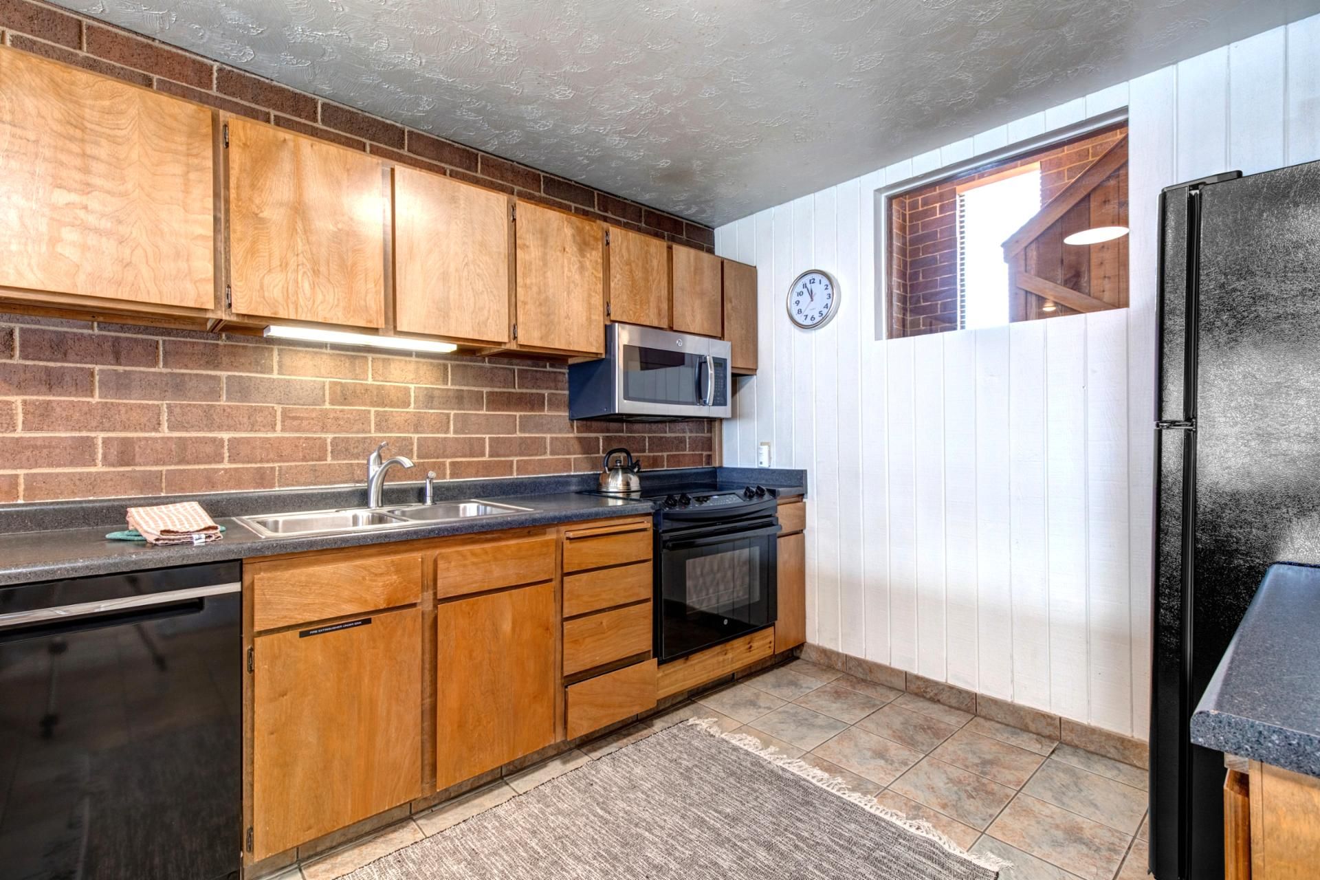 A kitchen with wooden cabinets, a stainless steel sink, a microwave, a stove, and a refrigerator.