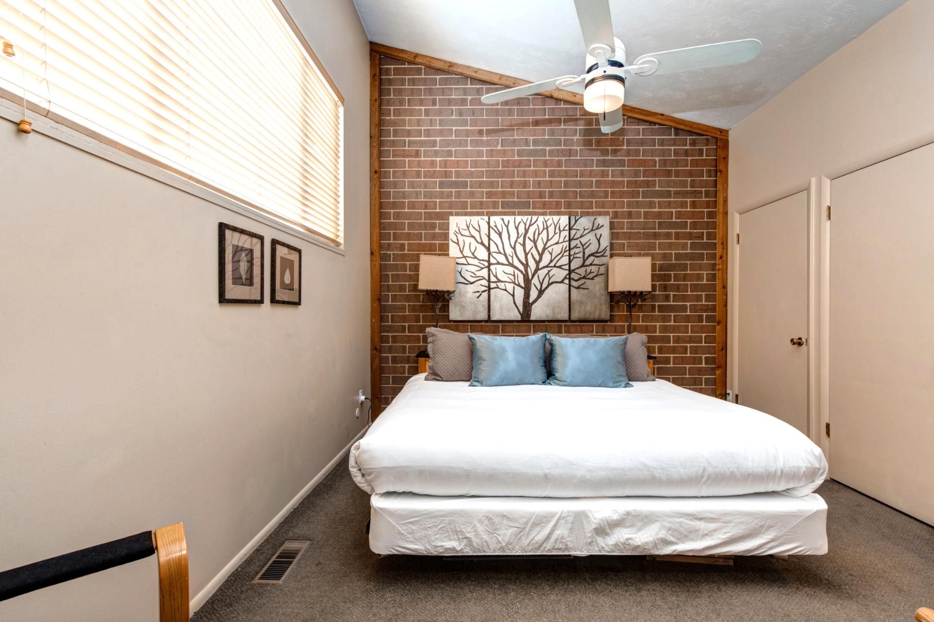 Ein Schlafzimmer mit einem Bett, einem Deckenventilator, einer Ziegelwand und einer Tür.