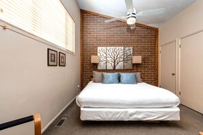 Ein Schlafzimmer mit einem Bett, einem Deckenventilator, einer Ziegelwand und einer Tür.