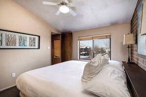 Ein Schlafzimmer mit Bett, Deckenventilator, Fenster mit Aussicht und Kunstwerken an der Wand.