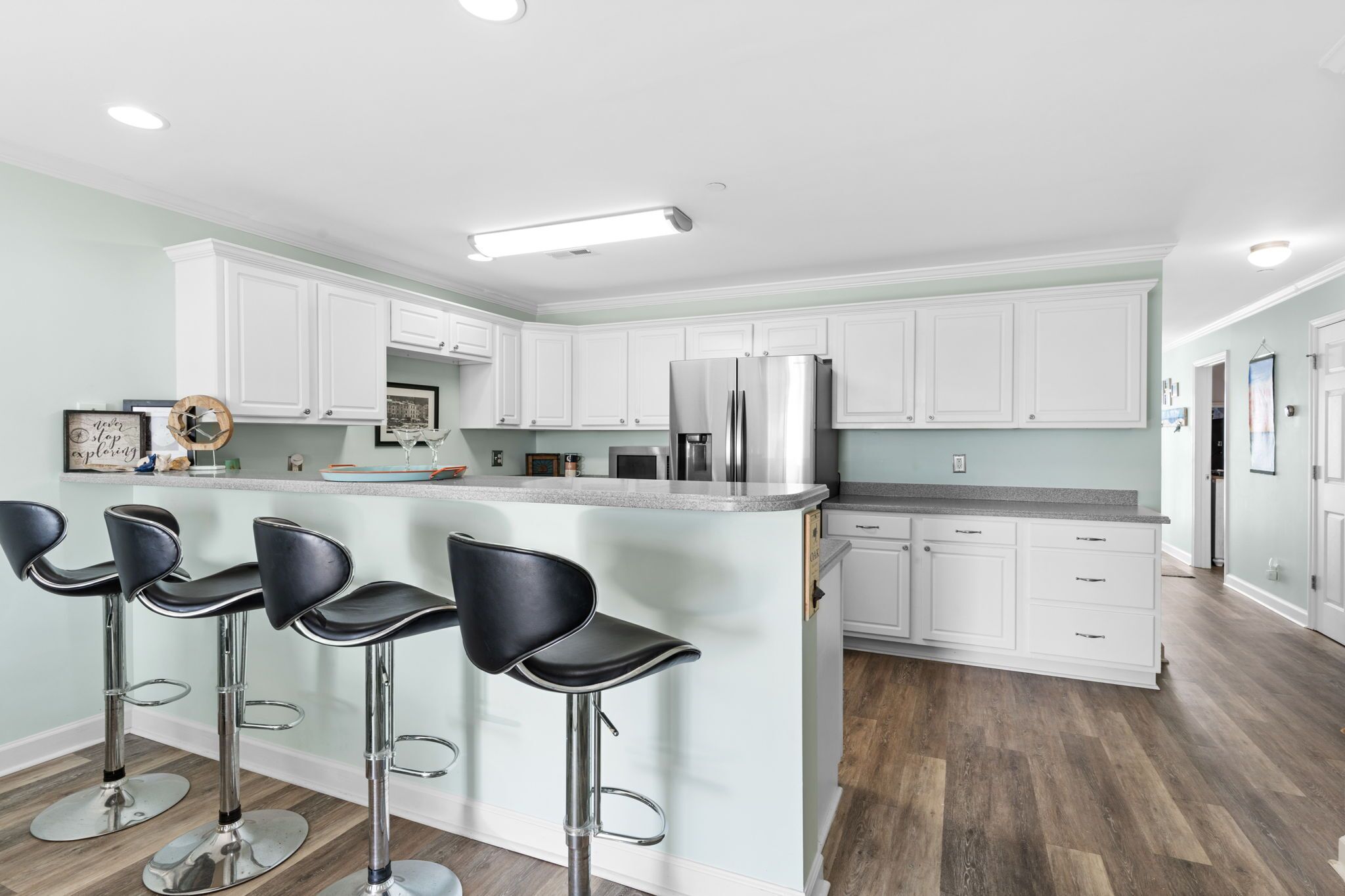 A modern kitchen with white cabinets, a stainless steel refrigerator, and three black bar stools.