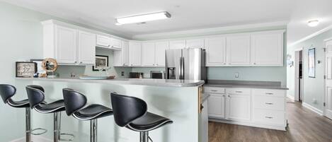 A modern kitchen with white cabinets, a stainless steel refrigerator, and three black bar stools.